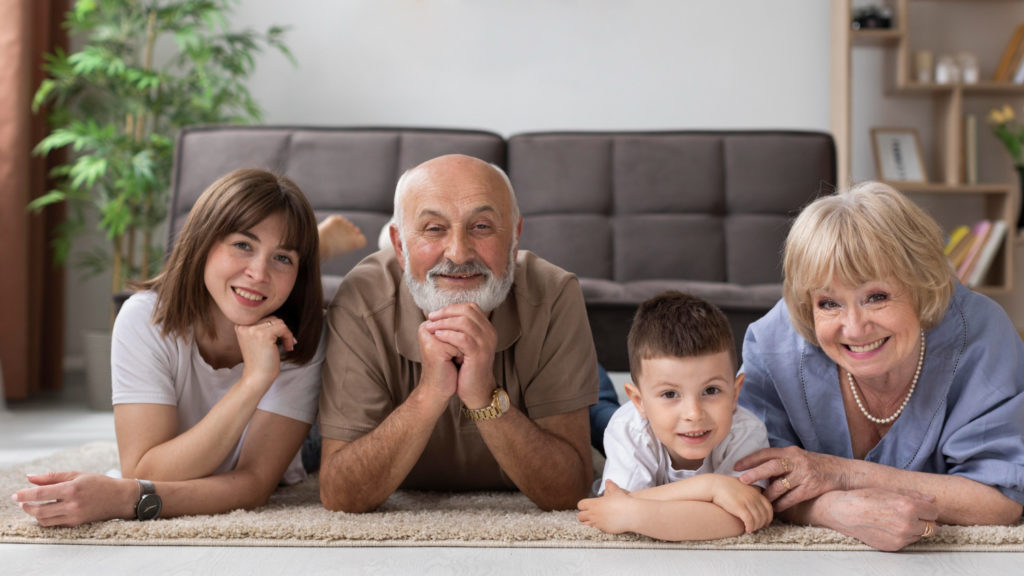 счастливые внучка, дедушка, внук, бабушка лежат на полу в гостиной и смотрят в камеру